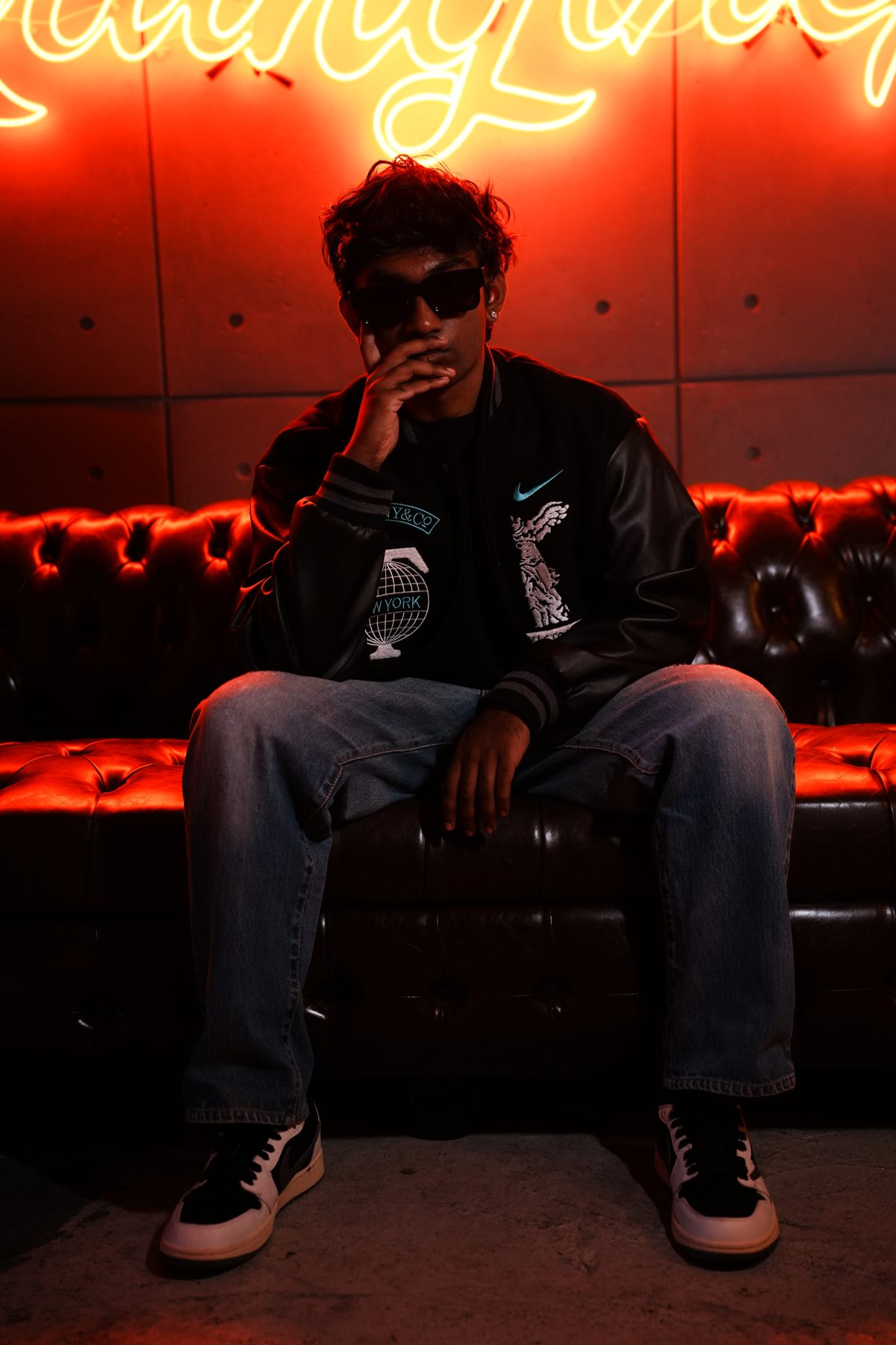 RYKARA seated on a leather sofa under red neon, press portrait 09